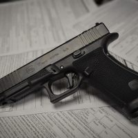 A black semi-automatic handgun rests on top of several firearm purchase application forms.
