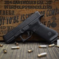 A black handgun rests on a surface with scattered bullets, beside a wooden crate marked with ammunition details.