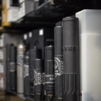 Close-up of various firearm suppressors and accessories displayed upright on shelves in a store.