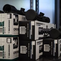 Stacked Vortex rifle scope boxes and scopes are displayed on a shelf in a store.