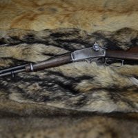 A lever-action rifle with a wooden stock rests on a spread of animal pelts with brown and tan fur patterns.